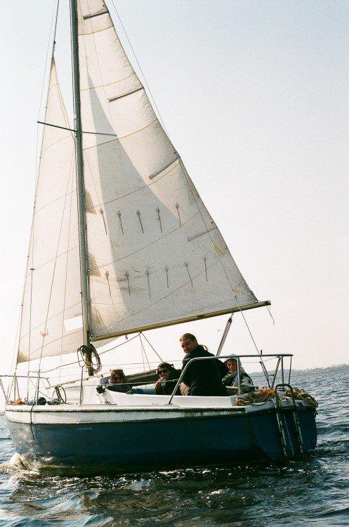 Un voilier avec plusieurs personnes à bord navigue sous une grande voile blanche